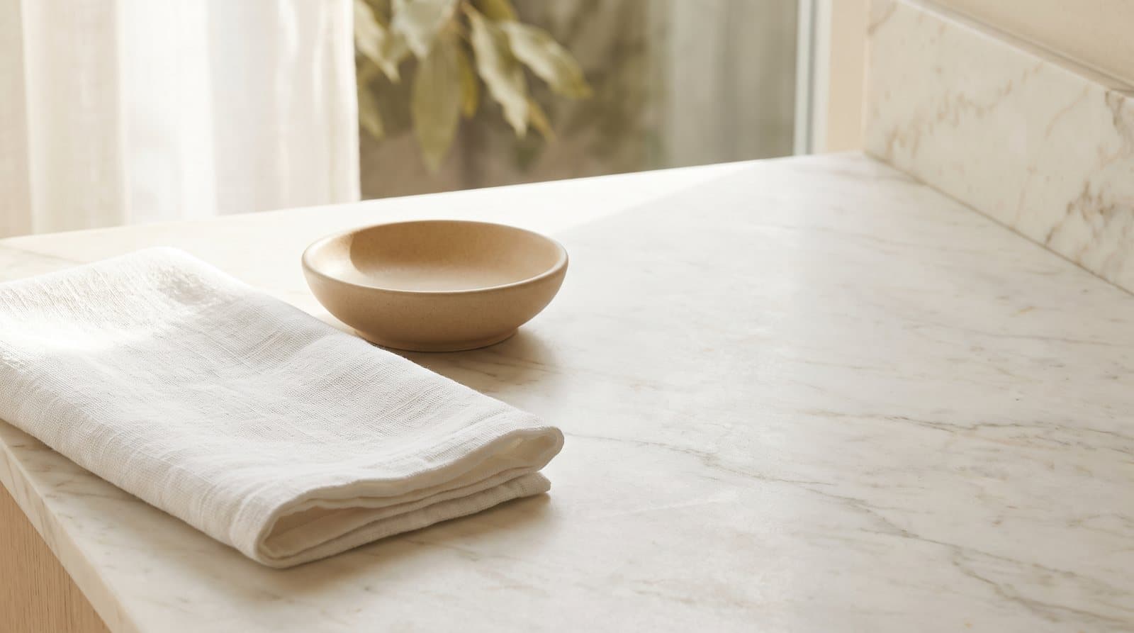 A folded linen towel and an empty ceramic dish on a marble counter in morning light.