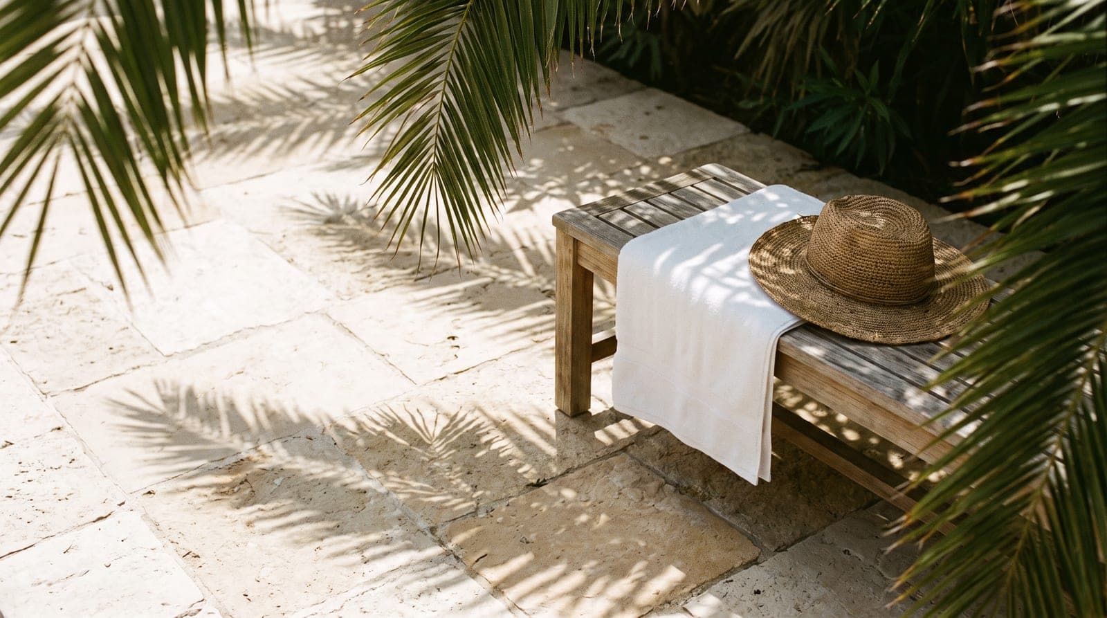 Dappled shade over a stone terrace with a folded towel and a straw hat on a bench.