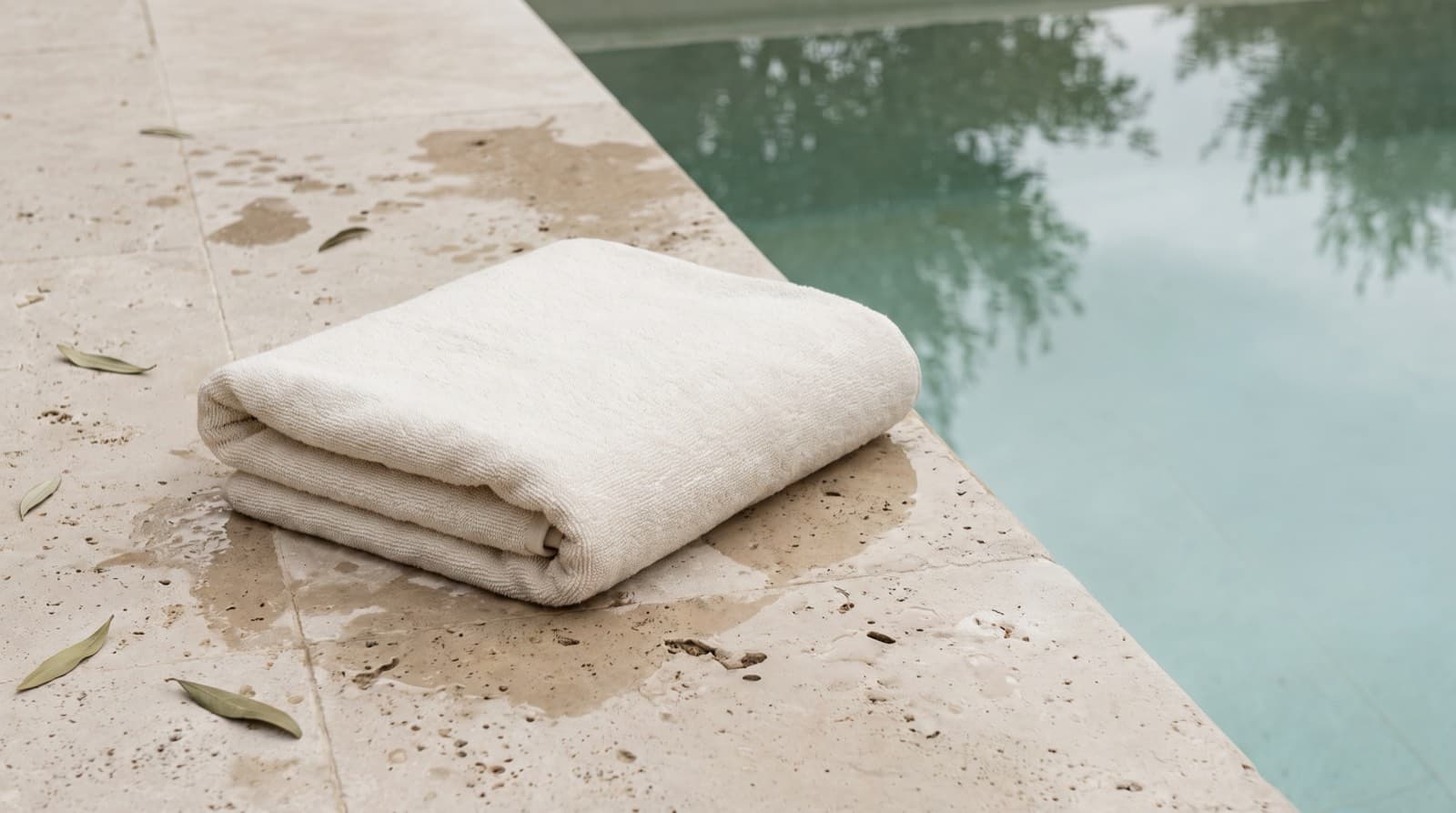 A folded plain towel on a wet stone pool deck beside the water.