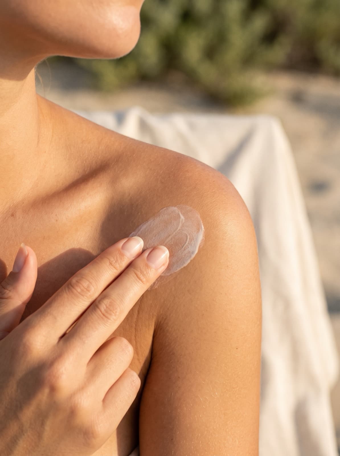 Fingertips rubbing Solvyn Shield into a shoulder in golden-hour light, the cream half blended from a pale bloom to an even satin finish