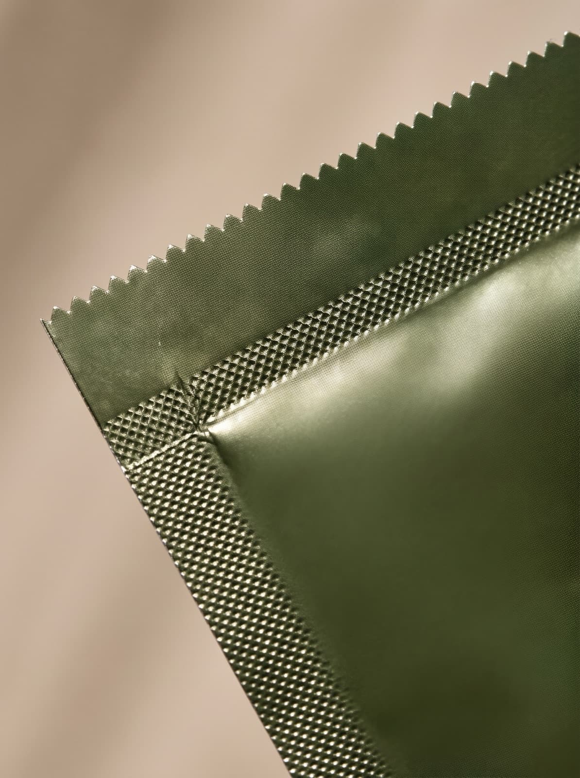 Macro detail of the serrated tear line and crimped foil seal along the top edge of an unopened Solvyn Shield sachet